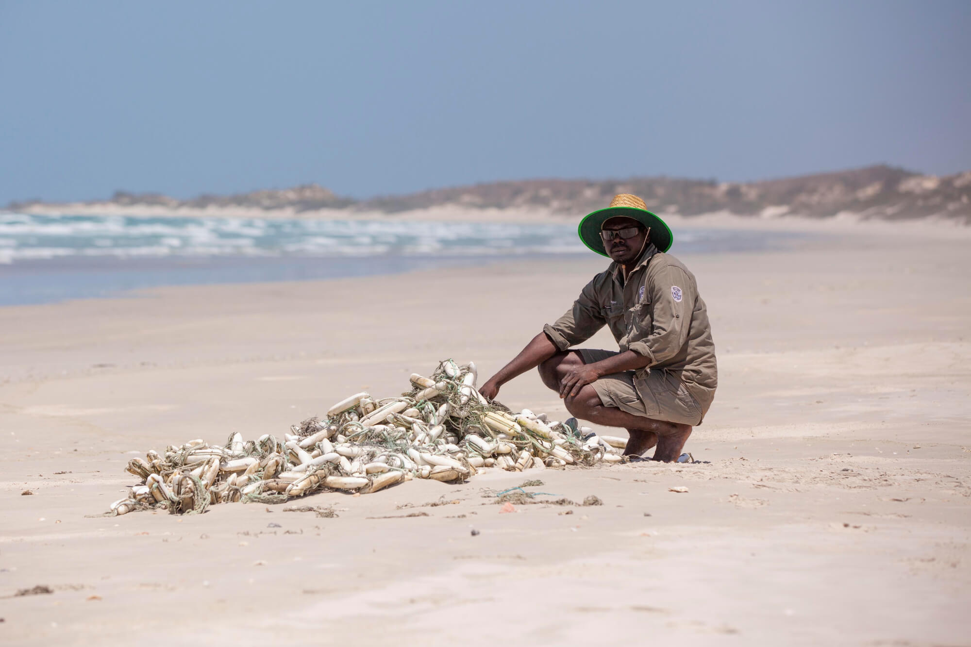 Man crouching down on beach near rubbish