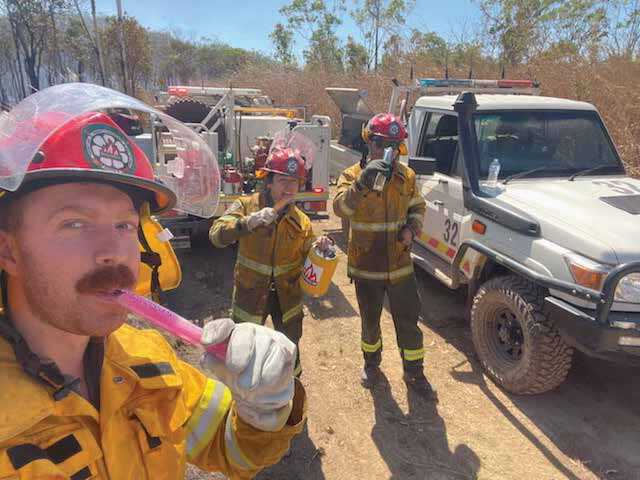 Firefighters in front of trucks, eating and drinking.